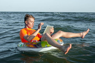 Man with ipad on inflatable ring in water