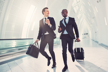 Two smiling businessmen rushing through an airport for a flight