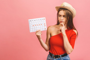 Portrait of a funny young girl holding periods calendar isolated over pink background.