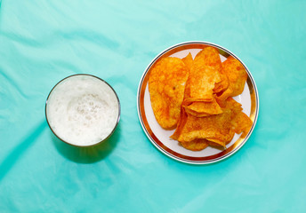 A glass of beer and a plate of chips on the table with a blue background.