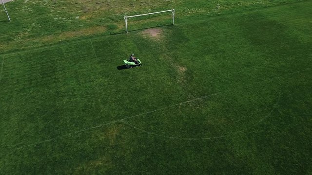 A man cleaning the soccer field mowing the grass on a lawn mower