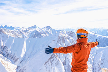 male person in red jacket wth spreaded hands looks to white mountains and snowy white peaks in the background. Mountains hug concept.