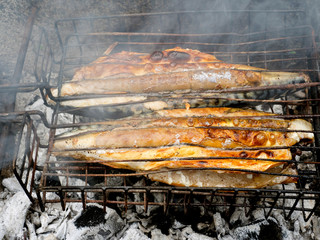 Fried fish. Hot mackerel fish on a grilling pan, with herb spices on coal fire