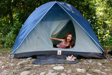 Portrait of emotional Little girl sits inside a tent and looking at camera. Grimacing child.