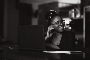 Beautiful Afro American girl in casual clothes is using a laptop and smiling while sitting in cafe