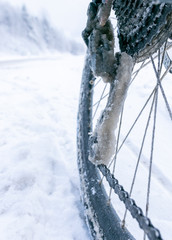 Close up of  frozen bicycle derailleur and chain with icy snowy road in the background. Cycling in extreme winter conditions.