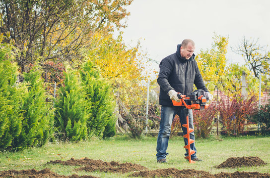 Man Digging Hole With Mechanic Machine Into Green Grass In The Garden, Works In The Garden