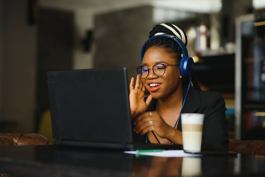 Attractive African American blogger with headphones and laptop communicating with followers in cafe