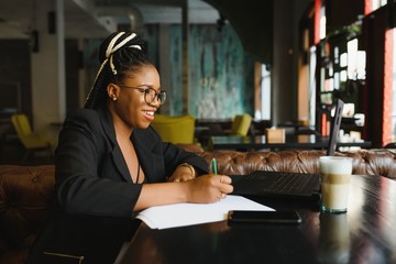 Beautiful Afro American girl in casual clothes is using a laptop and smiling while sitting in cafe