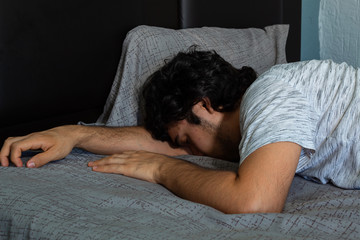 Young hispanic man with long curly hair taking a nap on a bed with gray sheets