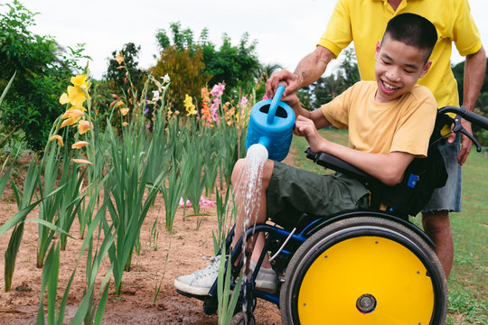 Asian special child on wheelchair and father watering the plants in flower garden,Daily activities happiness with family time in the home,Lifestyle in the education age and happy disabled kid concept.