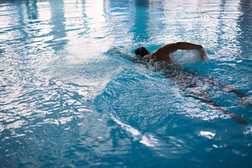athletic man swimming in  pool, blue water, reflection of windows in water, spray of water scatters from  movement of  man, selective focus