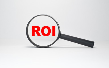 ROI RETURN ON INVESTMENT inscription in a magnifying glass on a boundless white background