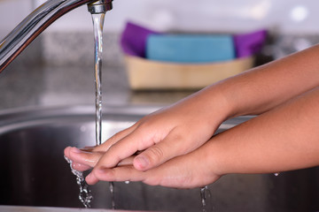 Girl rinsing her hands under the kitchen faucet. Washing her hands. Concept of cleaning.