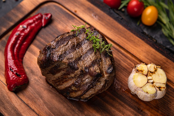 Fototapeta na wymiar American juicy steak on the board with spices, tomato and grilled vegetables. On a black table 