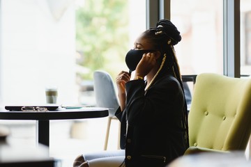 education, healthcare and pandemic concept - african student girl wearing face protective medical mask for protection from virus disease with laptop at cafe