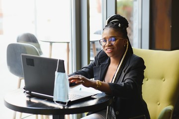 Focused female office worker using computer in coffee shop. African American business woman working on laptop in cafe and looking away. Internet technology concept