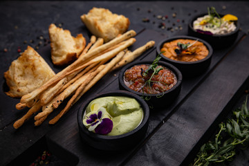Appetizers sauces with toasted bread and baked sticks are served on wooden stands. On dark concrete
