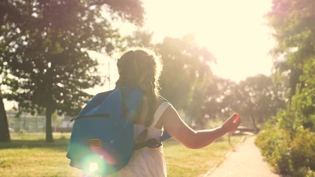 A schoolboy with a backpack and a book in the Park. A happy girl runs to school on the road. The child is in a hurry for lessons. The kid dreams of meeting friends.