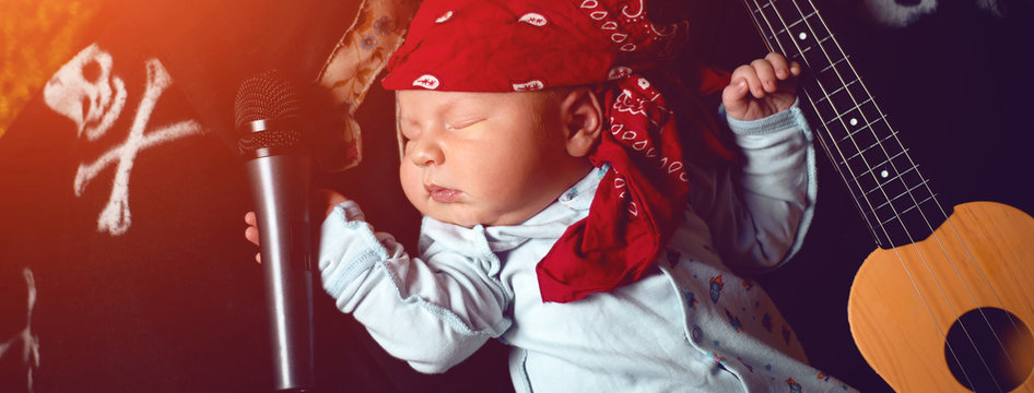 Baby In A Rocker Bandana Lies With A Guitar And A Microphone