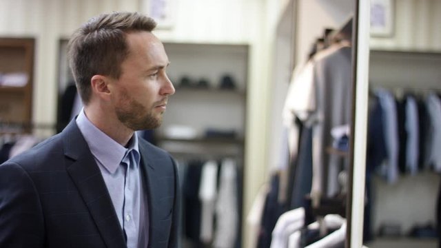 A side view slow motion close uo video of a dark haired business man standing in front of the mirror looking at himself and deciding on buyin a jacket
