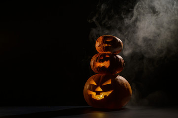 Three Halloween pumpkins stand on top of each other in a row. Traditional holiday decoration. Useful as a greeting card. Trick or treat.