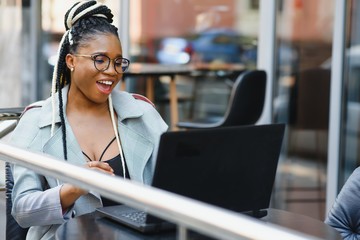 Focused female office worker using computer in coffee shop. African American business woman working on laptop in cafe and looking away. Internet technology concept