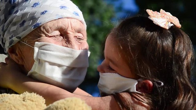 Joyful emotions of a small child and an old grandmother. Baby smile close up. Grandmother and child in protective medical masks close-up. The kid hugs his grandmother with sincerity