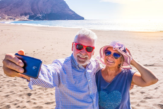 couple of mature people or pensioners enjoying their vacations and summer time together on the sand of the beach with the sea or ocean at the background - two retired senior taking a selfie smiling