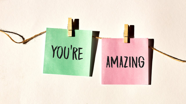 YOU ARE AMAZING text words inscription on yellow sticker note on white wall or table.