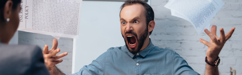 panoramic concept of angry and bearded man screaming while throwing in air documents near lawyer