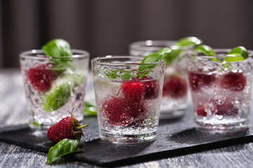 Fototapeta na wymiar Alcohol shots of berries cocktail with a raspberry and basil on black stone tray. Glass of sparkling water on wooden table
