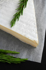 Cheese (brie) with rosemary on edible paper on a black background close up
