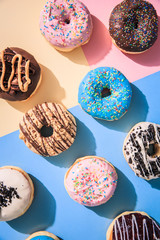 Top down view of colorful donuts flat lay on top of multicolored background.
