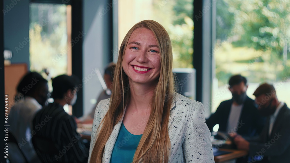 Wall mural Portrait of beautiful young 30s blonde business woman smiling at camera at modern light office background slow motion.