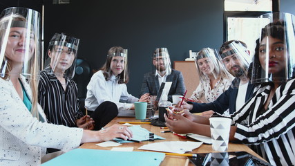 Office workplace safety measures. Happy diverse business team listening and clapping at camera, all wearing face shields - Powered by Adobe