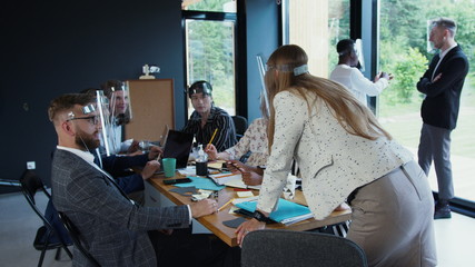 Happy young 30s blonde Caucasian female CEO leads multiethnic business team at office meeting, all wearing face shields.