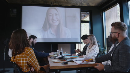 Group of multiethnic business people using projector for online web conference call with female coach at modern office.