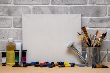 Set of artist accessories collection. Canvas, tube of oil paint, art brushes, palette knife lying on the wood table. Artist workshop background.