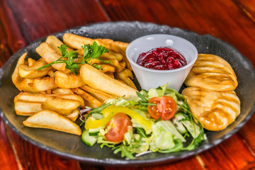Smoked cheese with french fries and cranberry jam with vegetable side dish. The food in the restaurant. Food styling and restaurant meal serving.