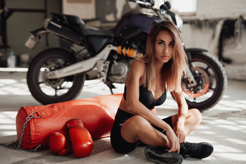 Plakat Sexy and attractive sportswoman posing in a light studio lying on the floor with a large orange punching bag. She is wearing a black and white tracksuit and she has orange boxing gloves.