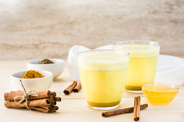 Detox drink. Golden milk with turmeric and cinnamon in glasses and ingredients for cooking on a wooden table.