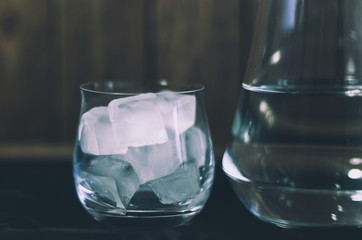 A glass of ice close up standing next to a jug in which cold water, objects on a background of wooden boards.