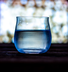 A glass of water stands on a wooden stand on a background of blurred retro lamps