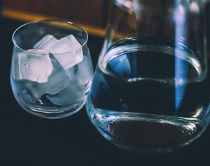 Glass of ice close up standing next to glass jug in which cold water