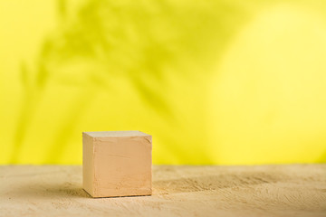 Mockup. Textured cube of beige surface on a yellow background with shadows from plants.
