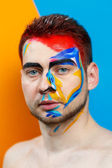 Makeup on the skin. Portrait of a young man with colored paint on a yellow background. Professional Makeup Fantasy Art Makeup