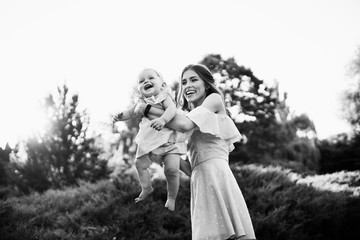 Fototapeta premium Overjoyed mother play with adorable daughter at the park, pretty woman hold baby girl in caring arms, smile, enjoy happy family moments, weekend outdoors, parenthood concept