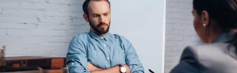 Obraz premium panoramic crop of displeased client sitting with crossed arms near lawyer