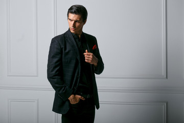 Profile portrait of confident young man in black suit with red silk scarf in pocket, over white...